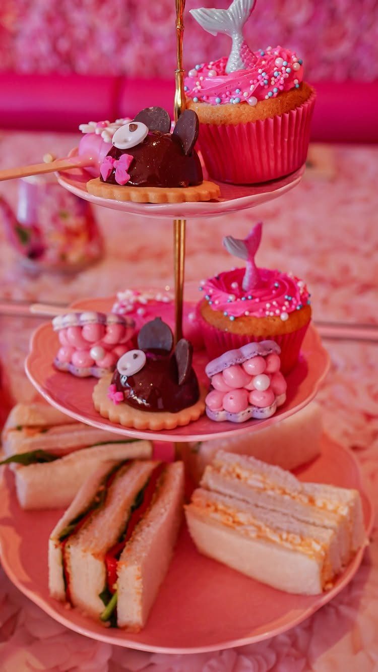 Three-tiered pink stand with finger sandwiches, mermaid cupcakes, and chocolate tarts.