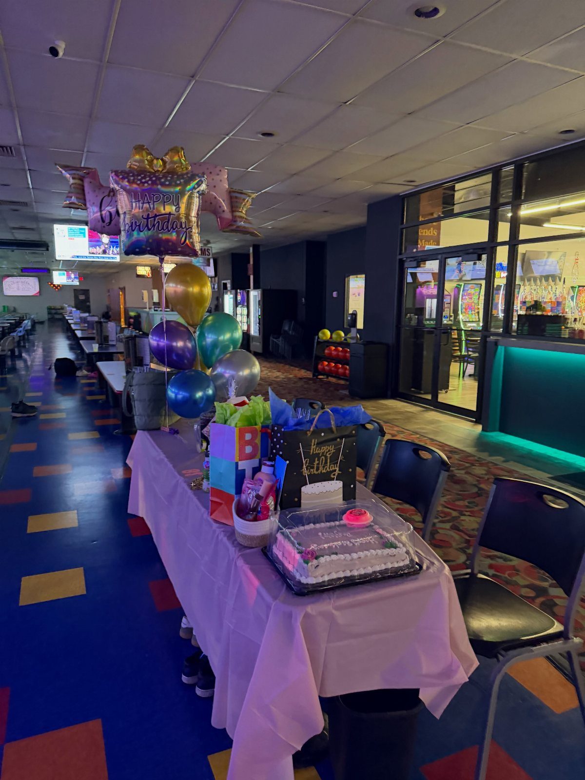 Birthday party table with cake and balloons inside a bowling alley setting
