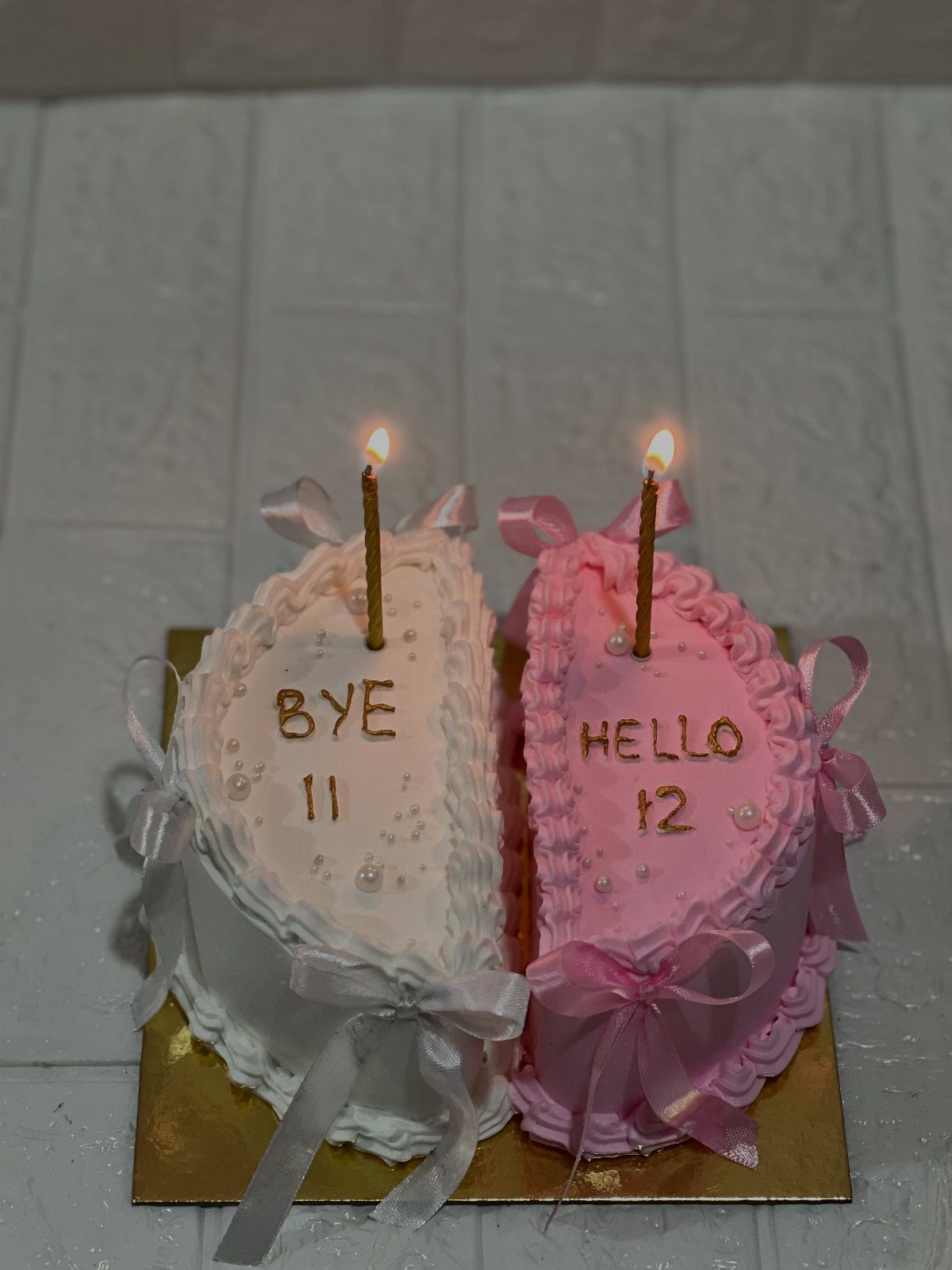 Two heart-shaped cakes, white and pink, celebrating a 12th birthday with lit candles.