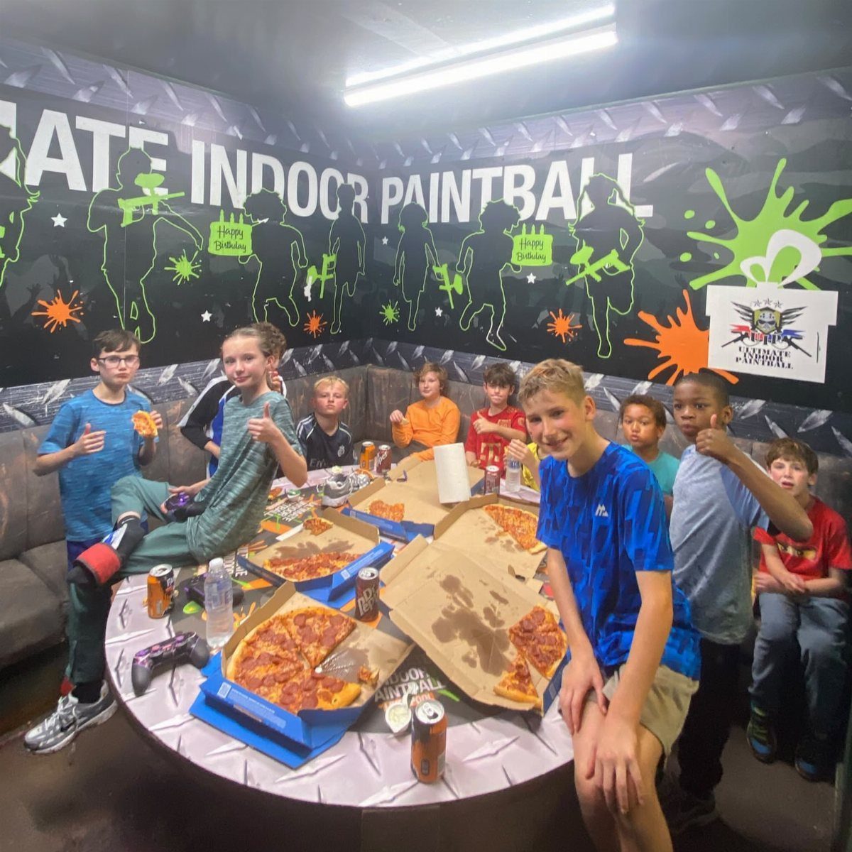 Group of boys eating pizza in an indoor paintball venue party room.