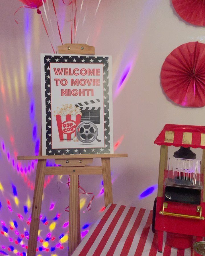 Movie night welcome sign on an easel with a red popcorn machine.