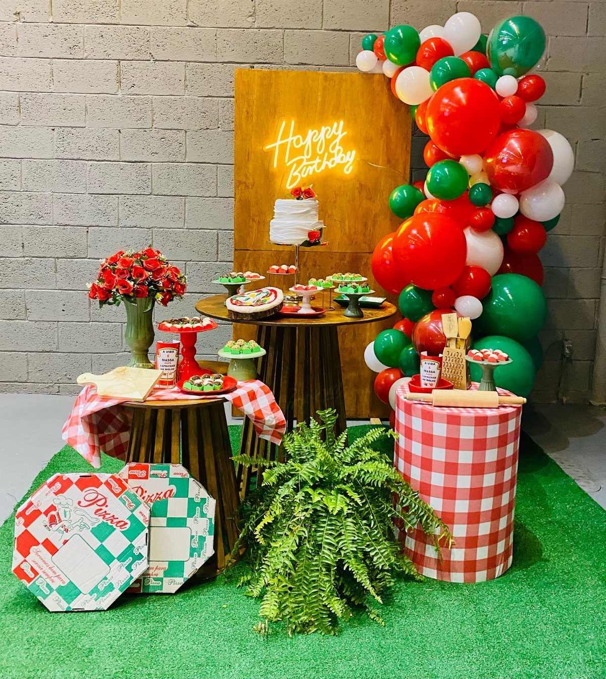 Birthday party setup with pizza boxes, red checkered cloths, and Italian-colored balloons.