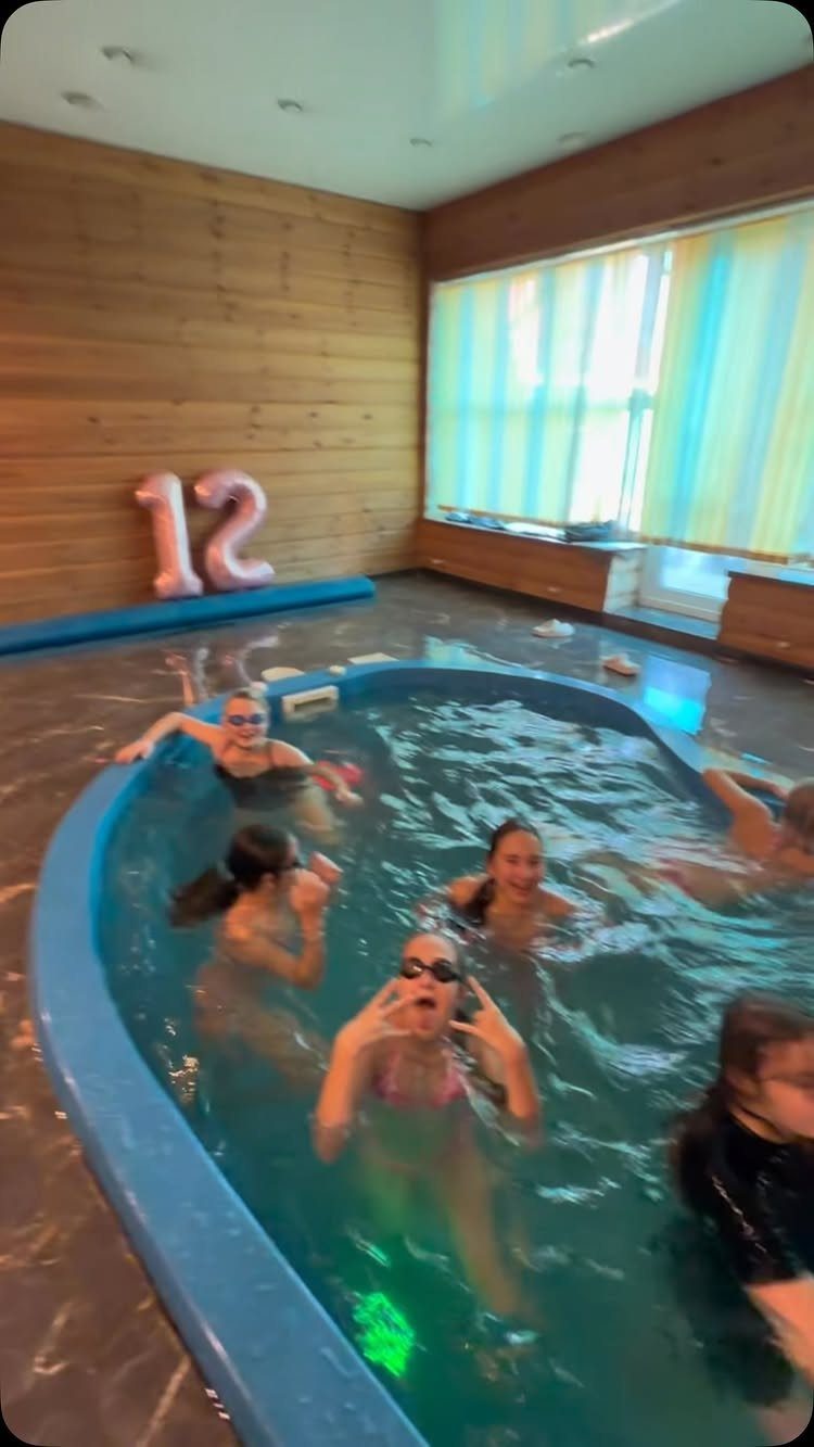 Young girls laughing in a blue indoor pool with a number 12 balloon.