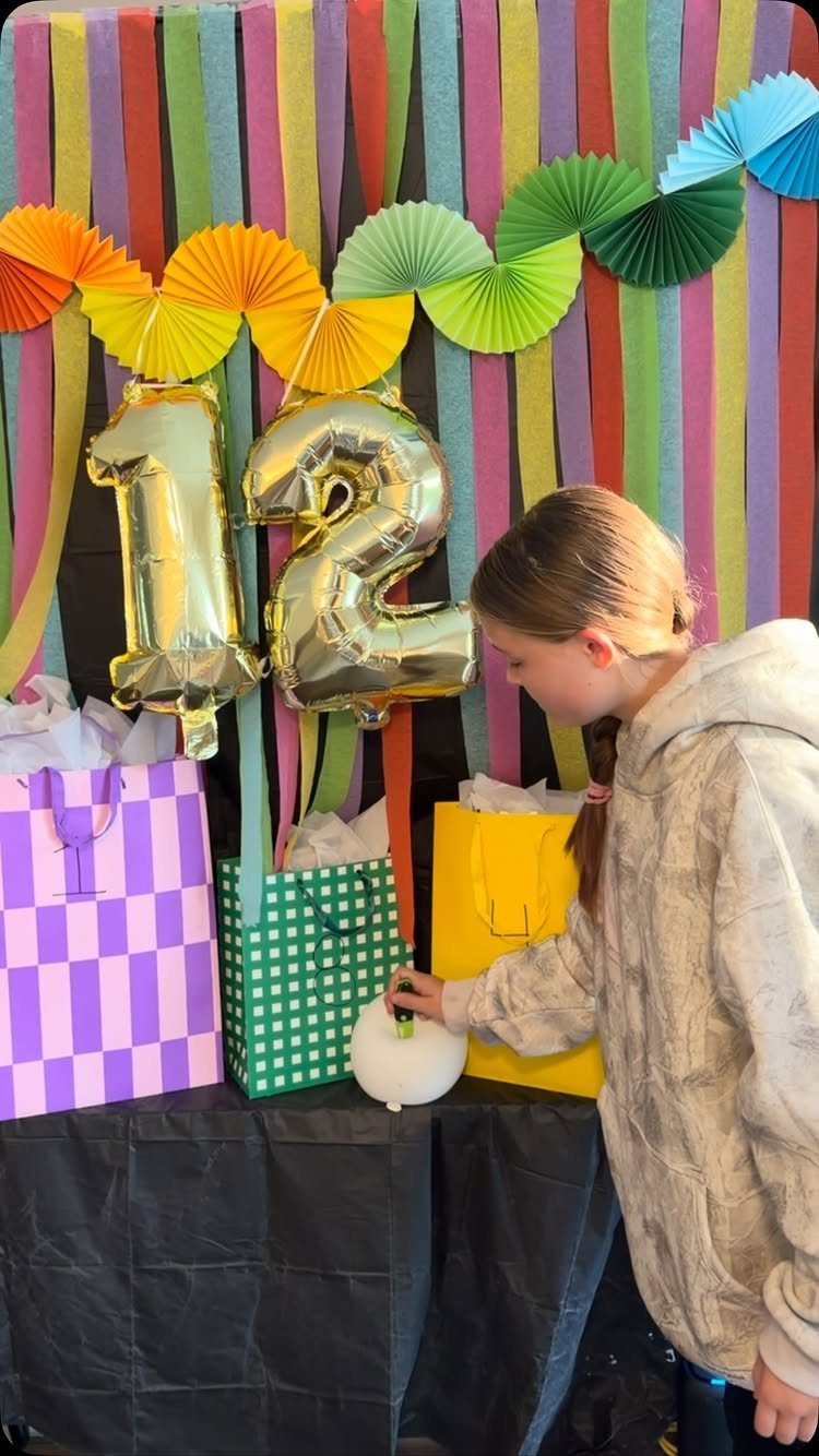 Girl standing by a birthday backdrop with gold 12 balloons and gift bags.