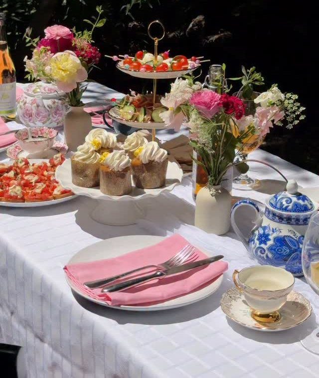 Elegant outdoor tea party table with cupcakes, floral arrangements, and blue porcelain teapot.
