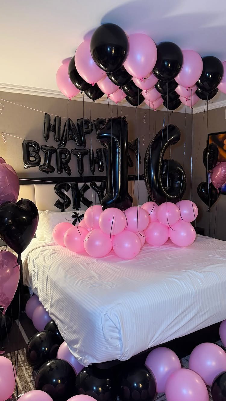 Pink and black birthday balloons decorating a bedroom with a large number 16