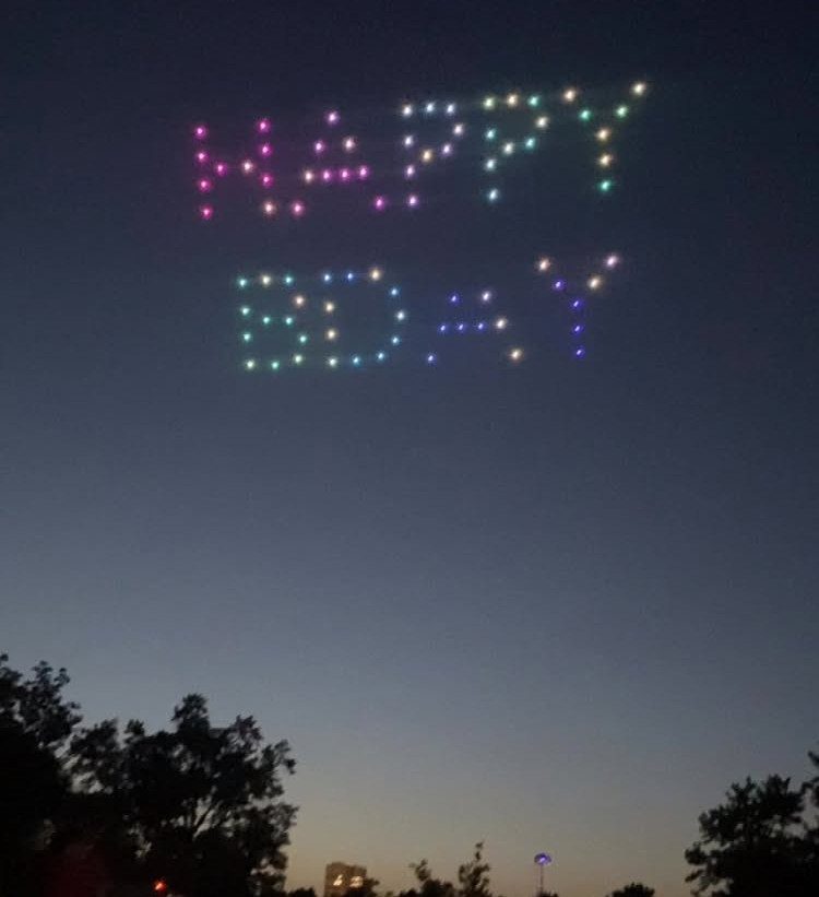 Colorful drone lights spelling Happy Bday in a dark evening sky