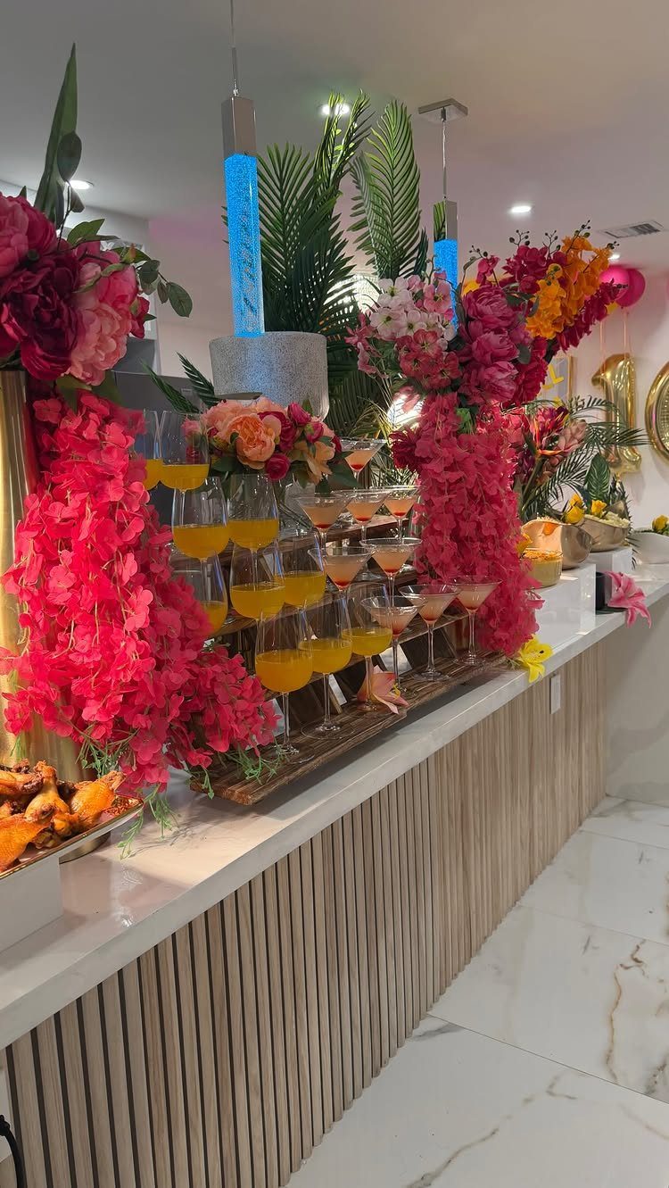 Cocktail towers and vibrant floral arrangements on a white party beverage station