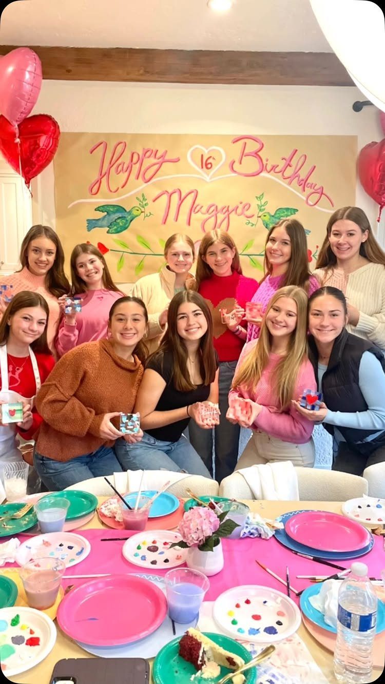 Teenage girls posing at a 16th birthday party with painting supplies and banner.