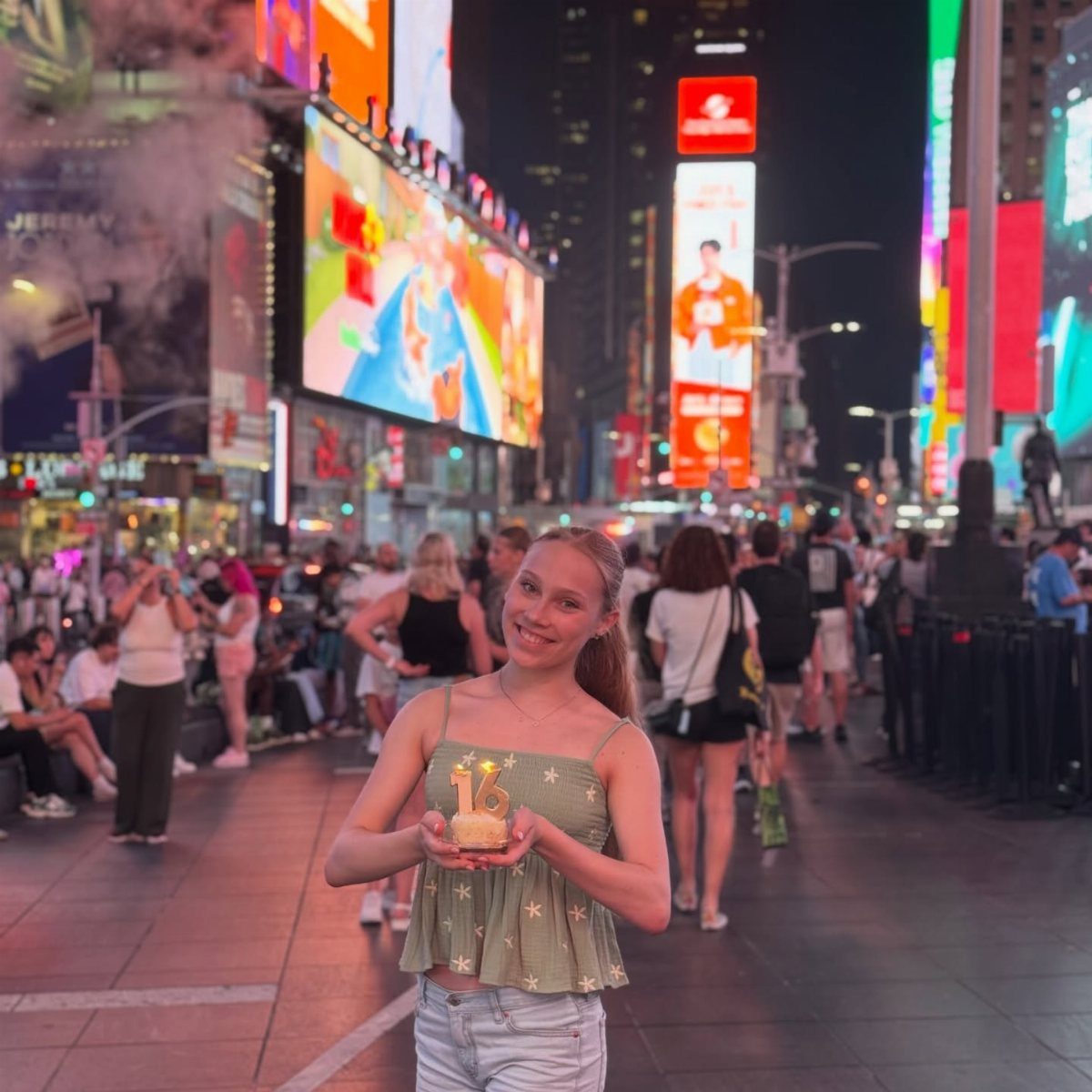 Teenage girl holding a birthday cake with 16 candle in Times Square NYC