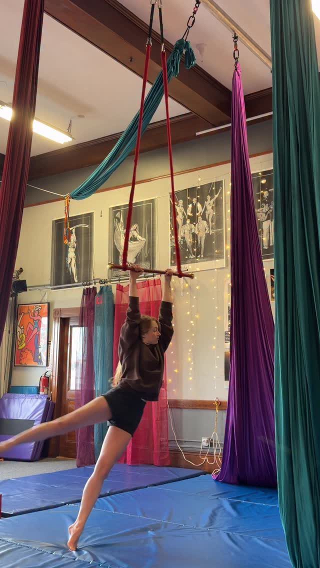 Young woman performing on a trapeze bar in an aerial arts studio