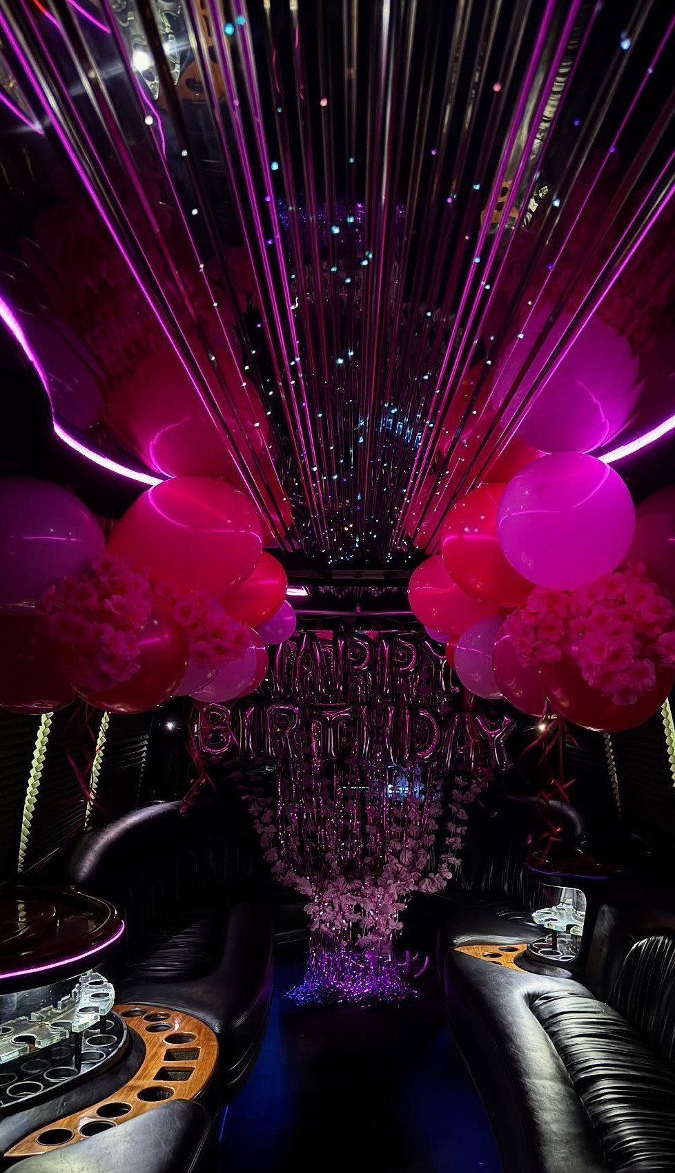 Party bus interior with pink balloons, purple neon lights, and birthday foil balloons.