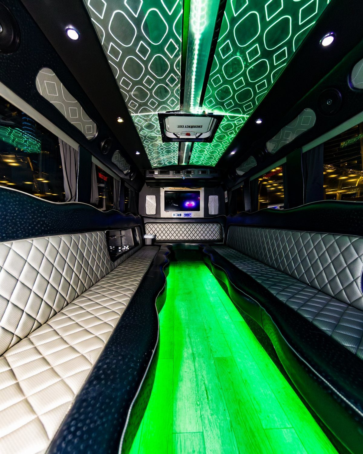 Party bus interior with diamond-stitched leather seating and vibrant green neon lighting.