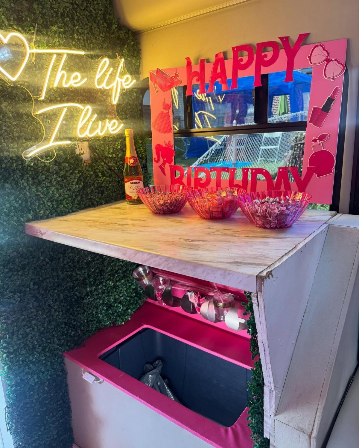 Party bus interior with pink birthday decorations, neon sign, and a refreshment counter.