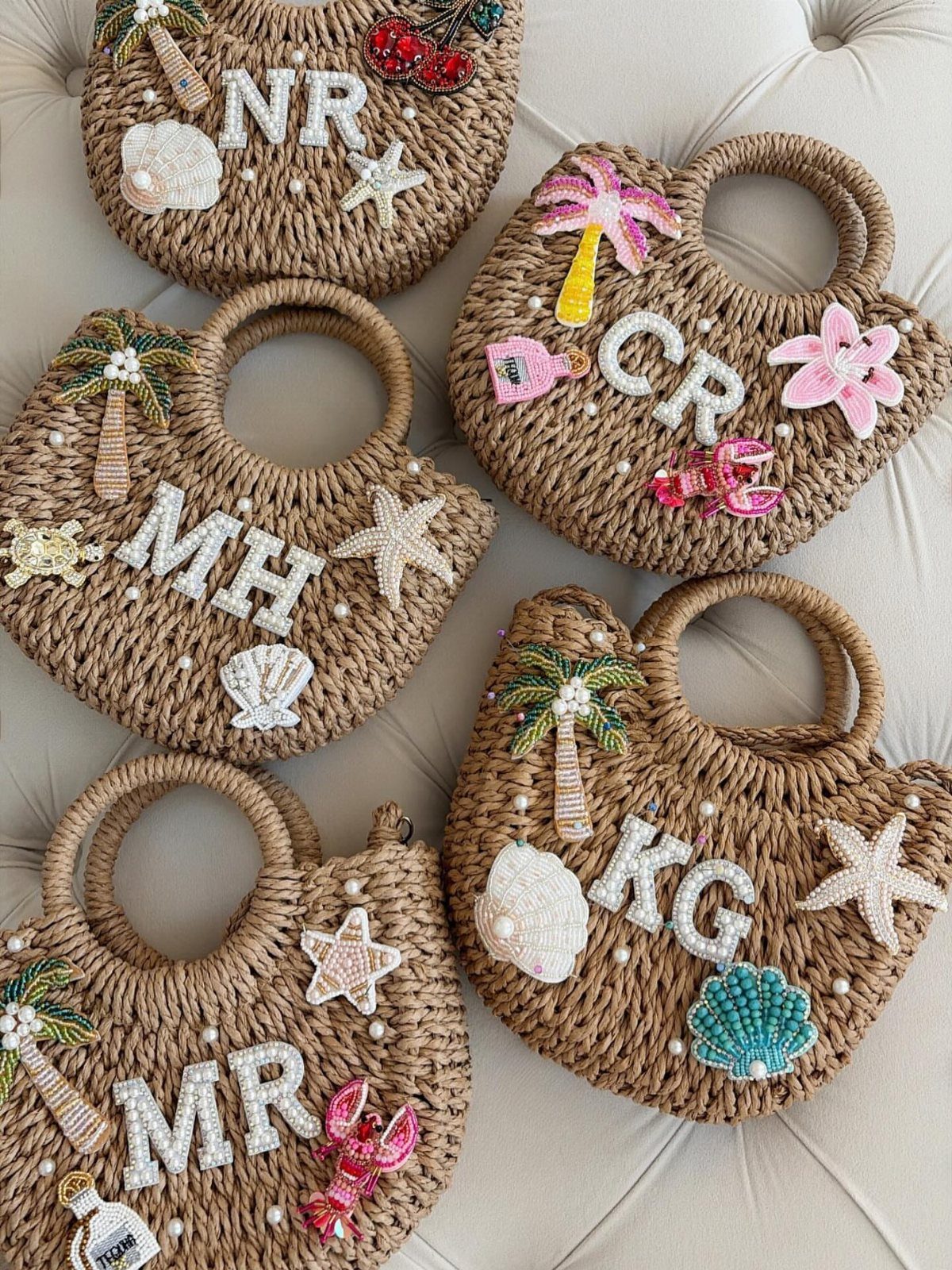 Woven straw handbags decorated with beaded initials and colorful beach-themed embellishments.
