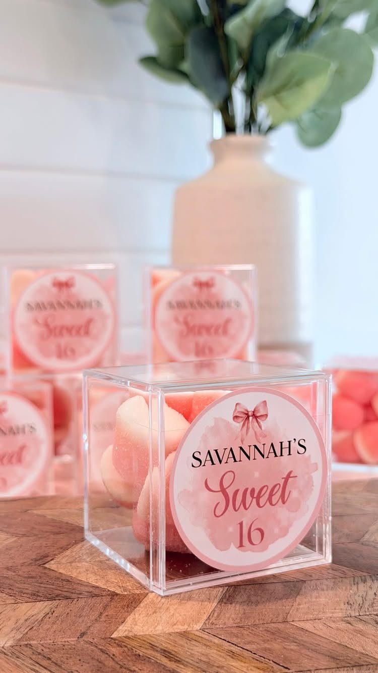 Acrylic favor boxes with pink candies and Sweet 16 labels on wooden table