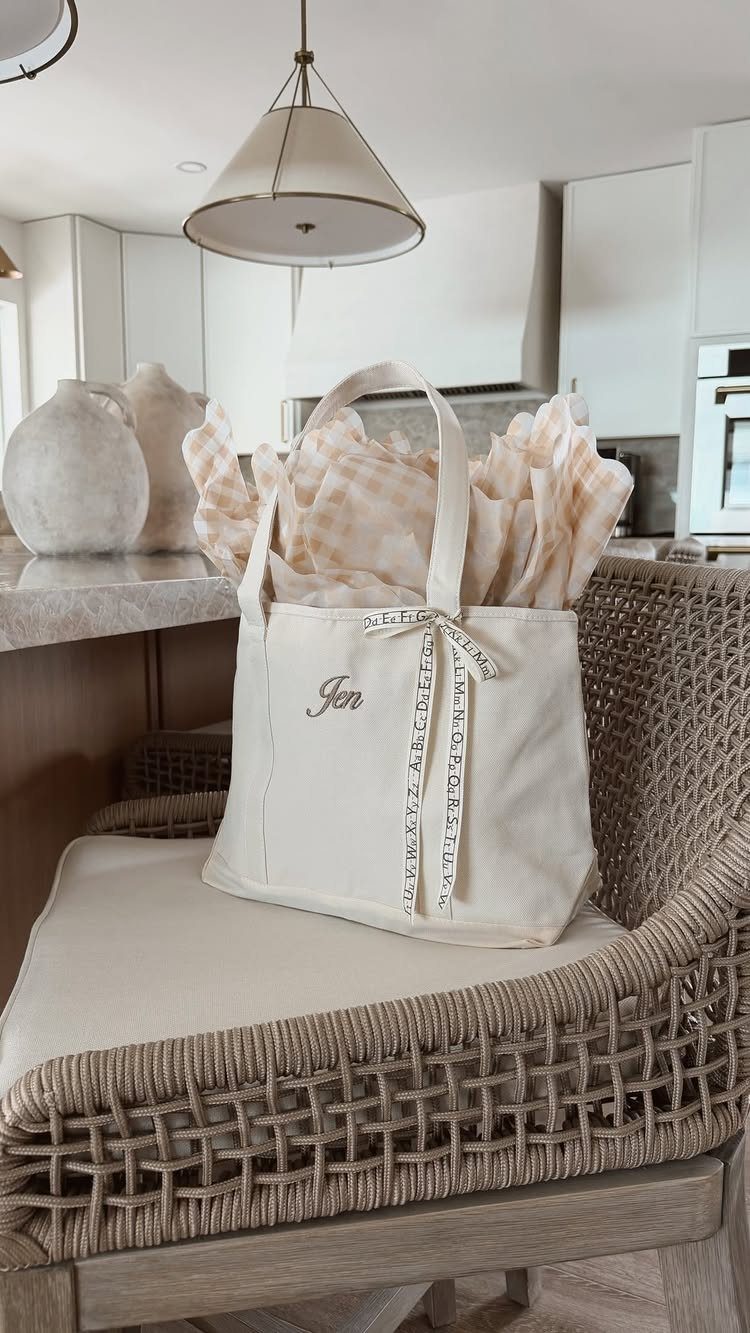 Cream canvas tote bag with Jen embroidered on it sitting on a chair
