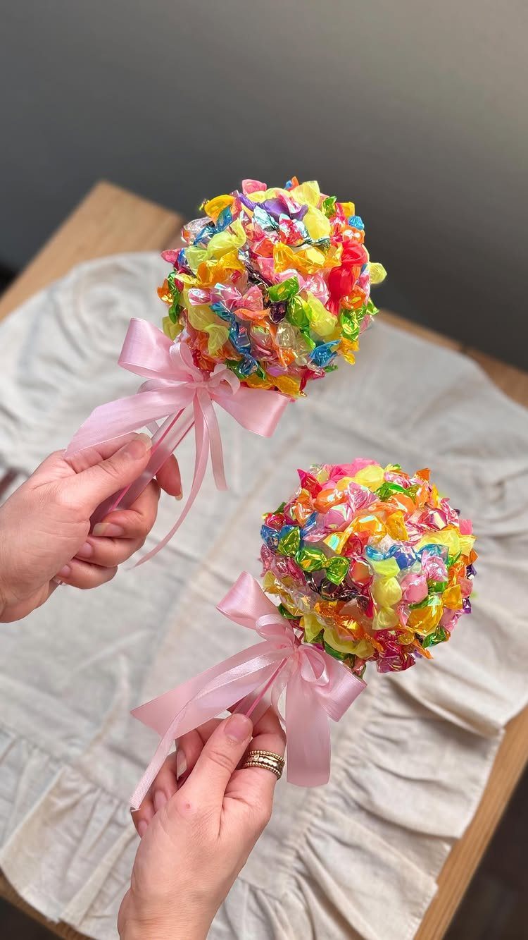 Colorful candy wands with pink bows held by hands over white fabric.