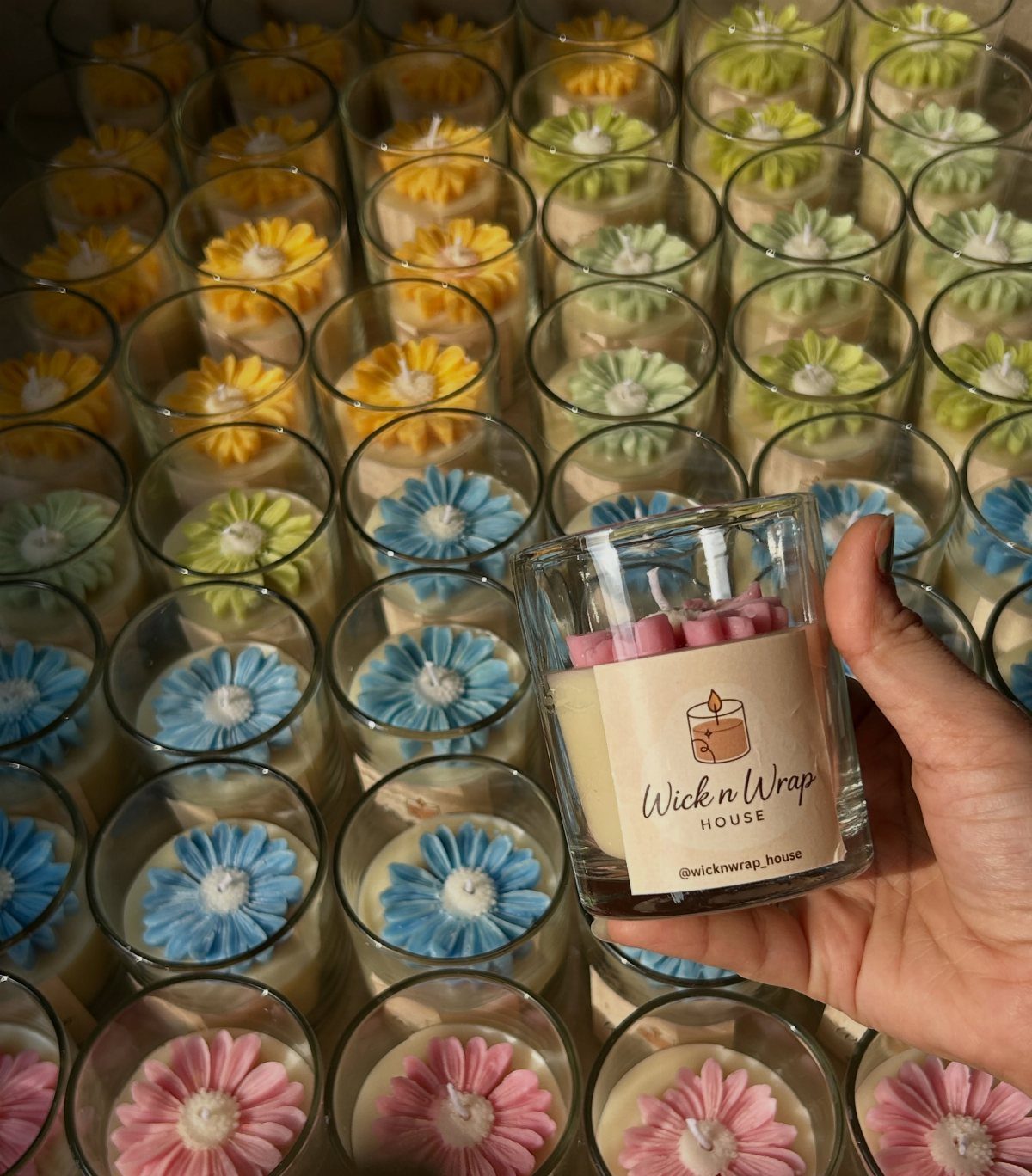 Hand holding a mini scented candle with a pink wax flower topper.