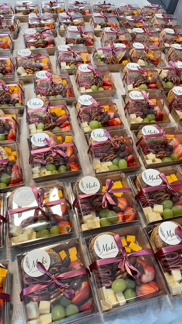 Clear plastic snack boxes filled with fruit, cheese, and chocolate tied with pink ribbons.
