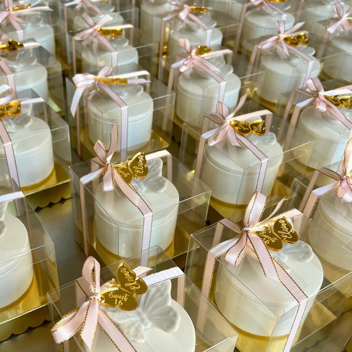 White candles in clear gift boxes with pink ribbons and gold butterfly charms.