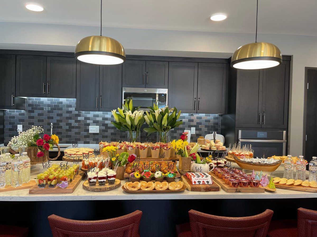 Dessert bar station on a kitchen island with donuts, cupcakes, and fruit skewers.