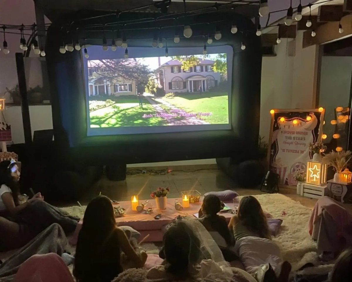 People relaxing on a rug watching a movie on a large projector screen.