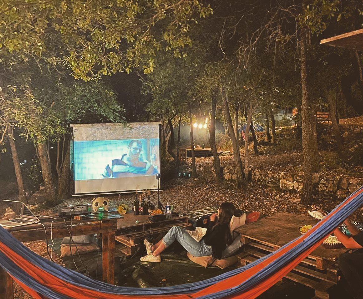Projector screen showing a movie in a wooded backyard with lounge seating.