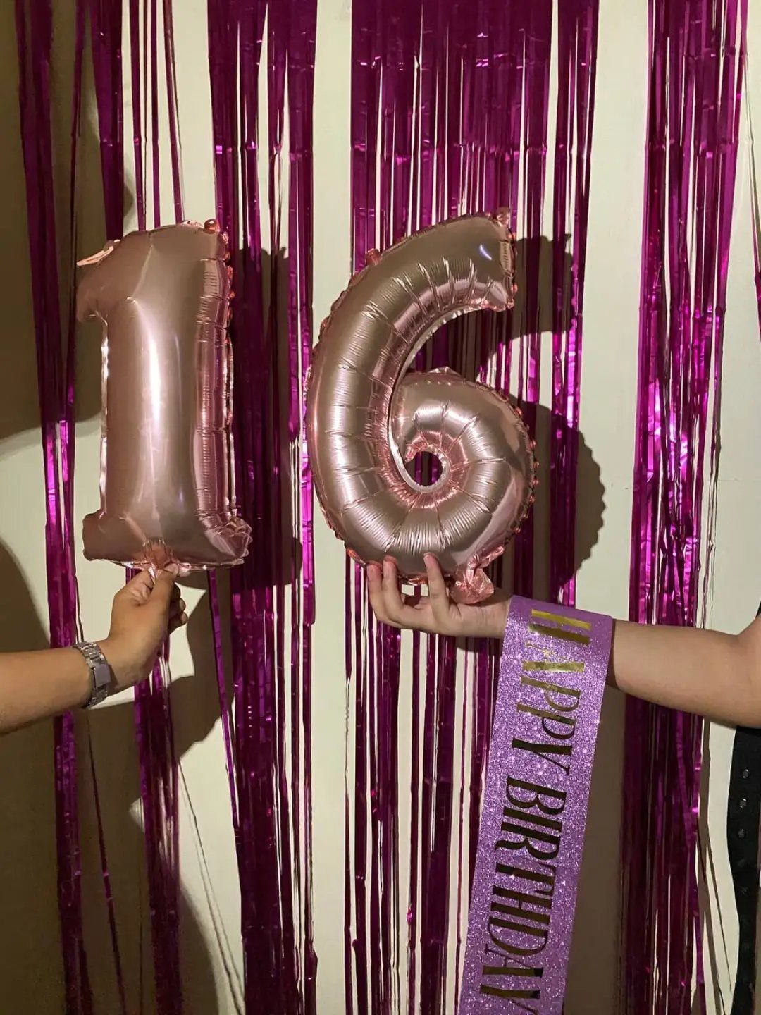 Rose gold 16 balloons held against a purple foil fringe birthday backdrop.