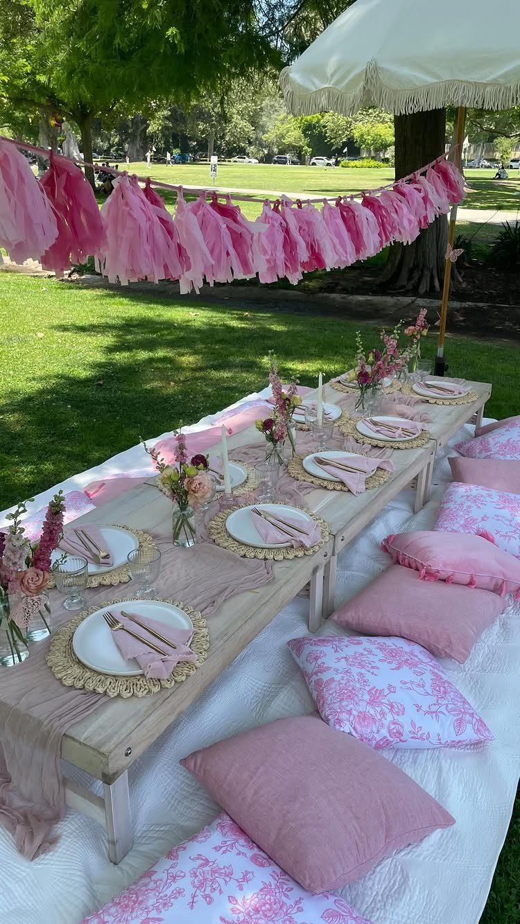 Low wooden party table with pink decorations and pillows in a sunny park
