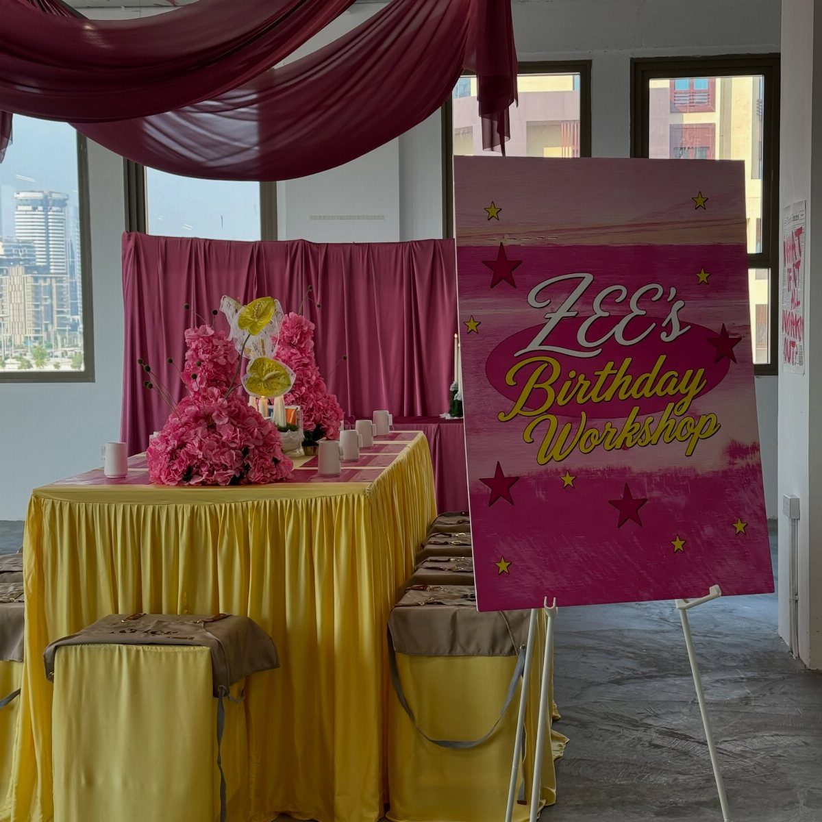 Yellow draped table with pink flowers and a birthday workshop sign in a room