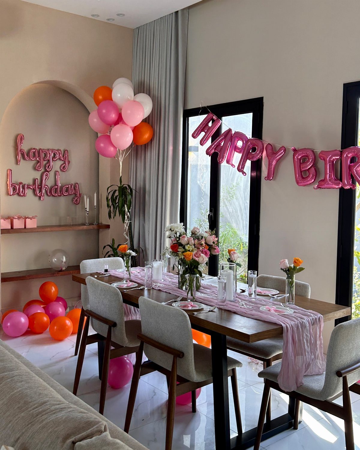 Decorated dining room with pink balloons, flowers, and a happy birthday neon sign.