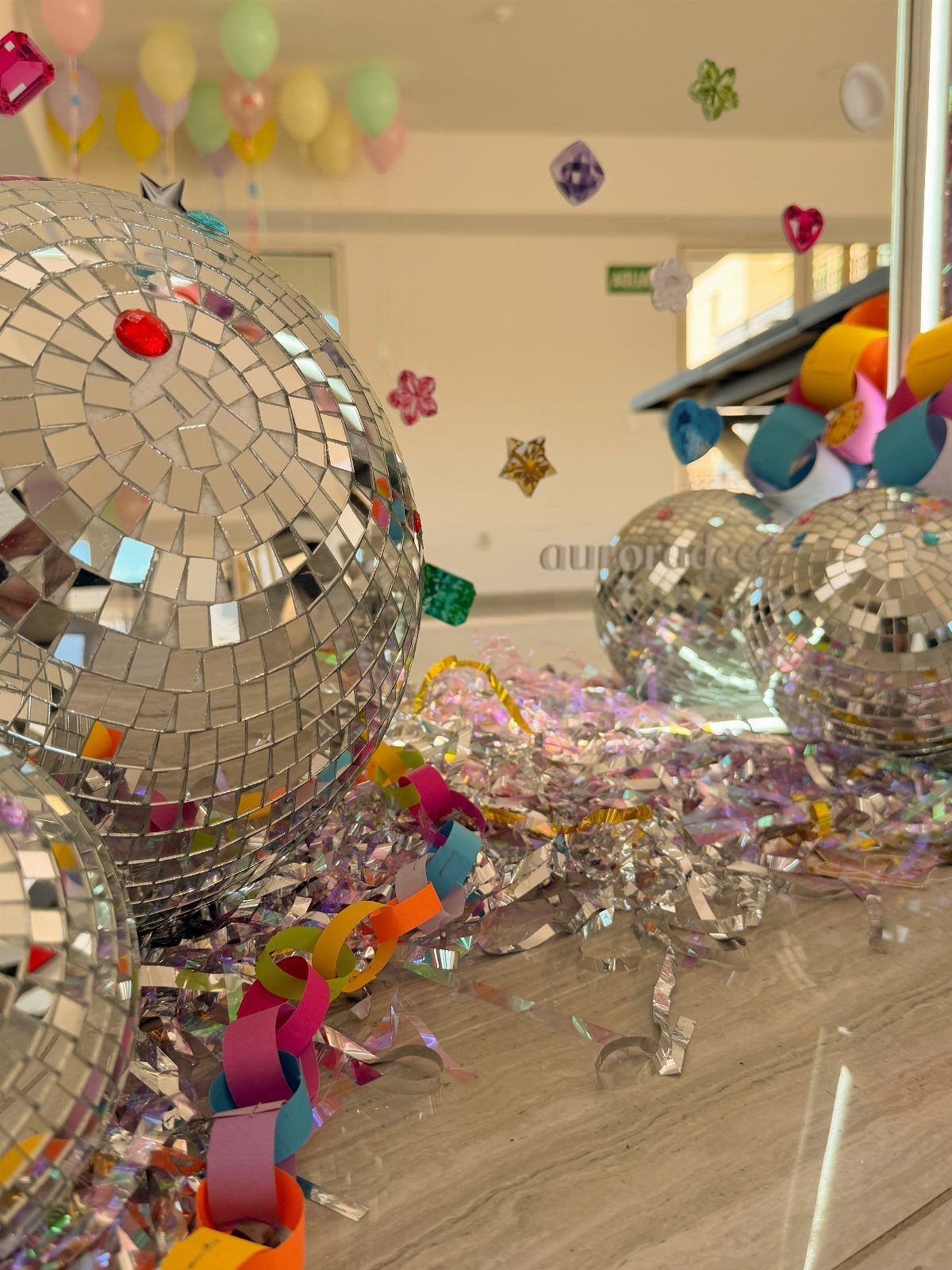 Mirrored disco balls on a floor covered in iridescent silver confetti and colorful chains.