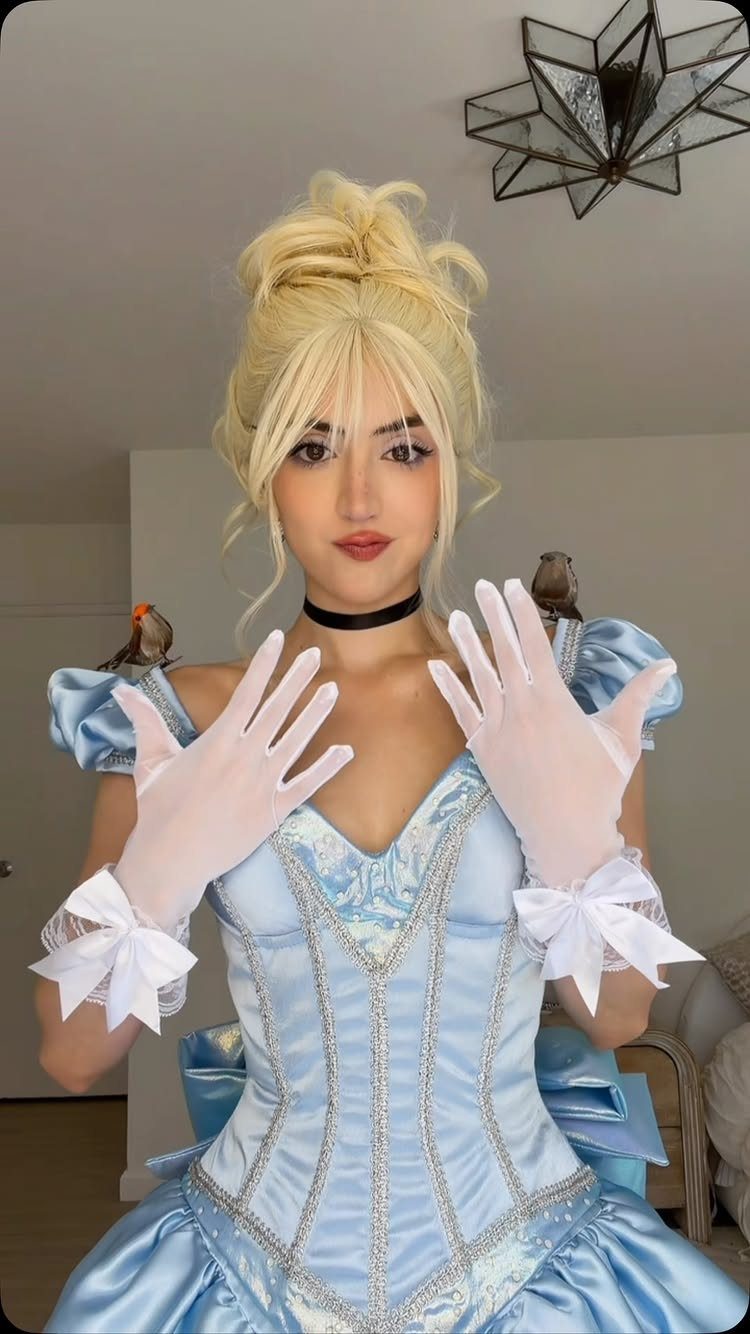 Woman in a light blue Cinderella ballgown and white gloves posing indoors.