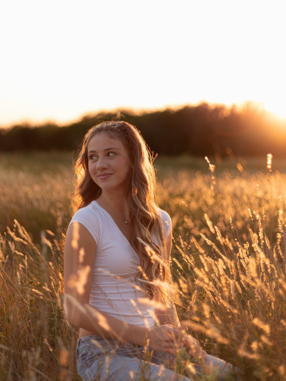 Teenage girl sitting in a golden grass field during a warm sunset glow.