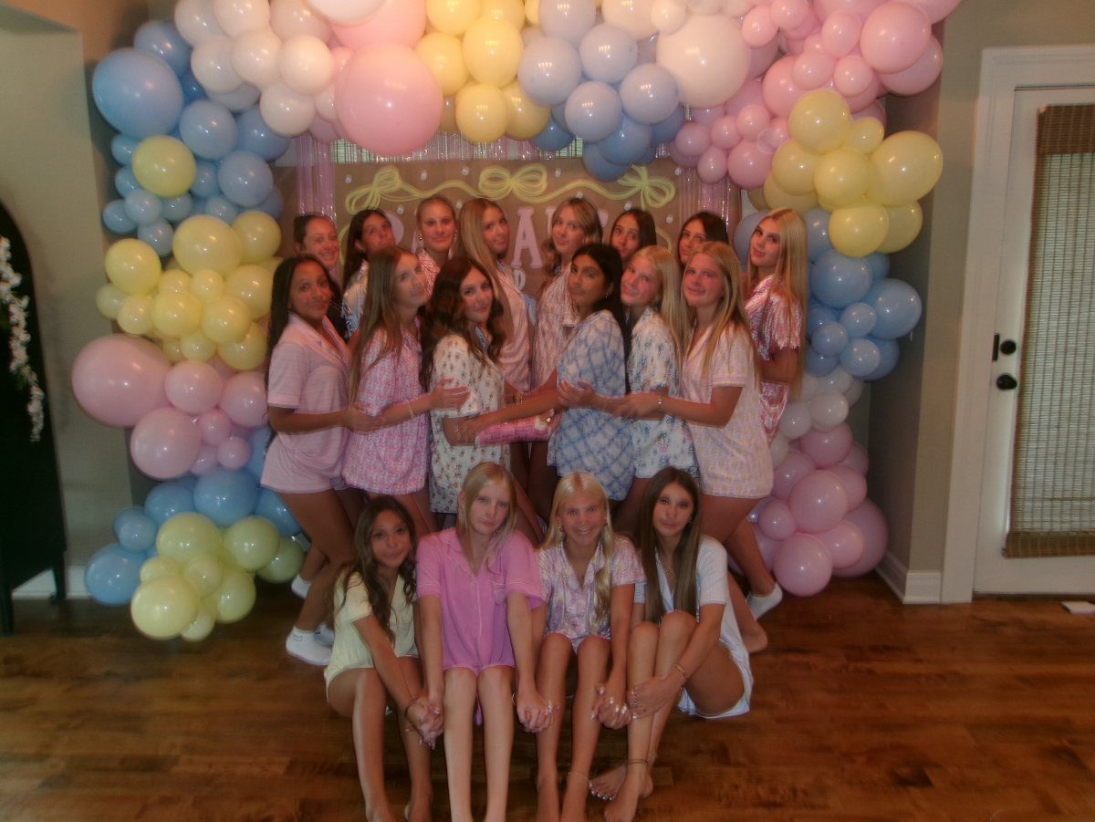 Teenage girls in pastel pajamas posing before a colorful balloon arch indoors.