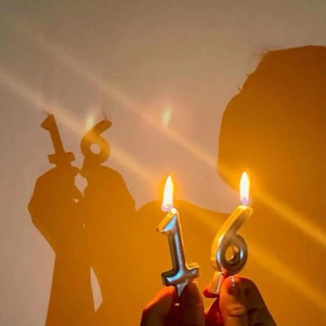 Lit gold number 16 candles casting a large shadow on a wall