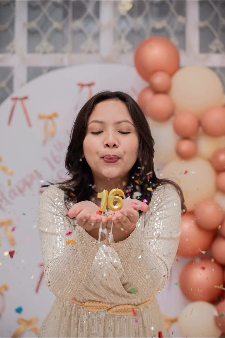 Teenage girl in gold sequin dress blowing confetti with number 16 candles.