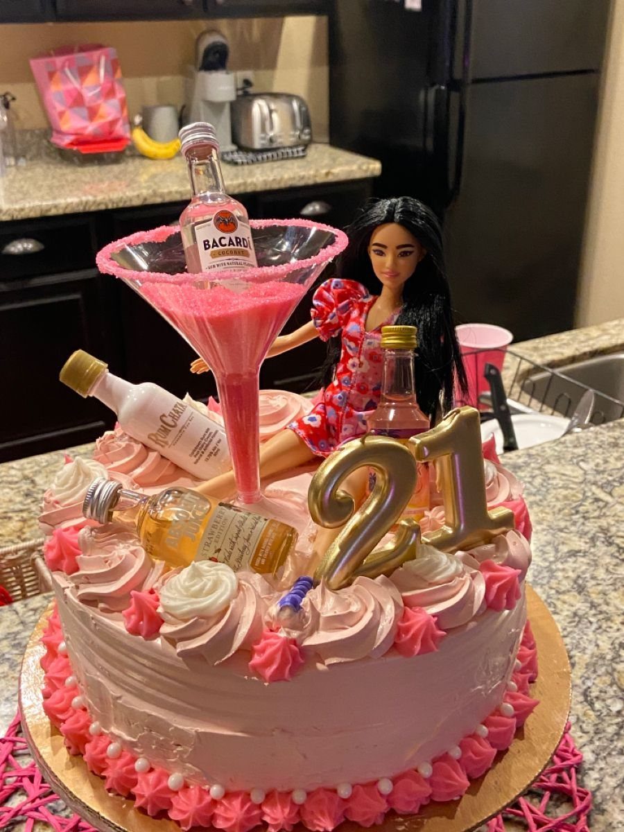 Pink birthday cake with a Barbie doll, martini glass, and gold 21 balloons.