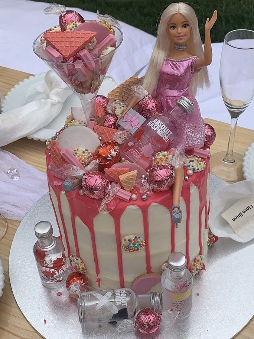 White cake with pink drip icing topped with a Barbie doll and candies.