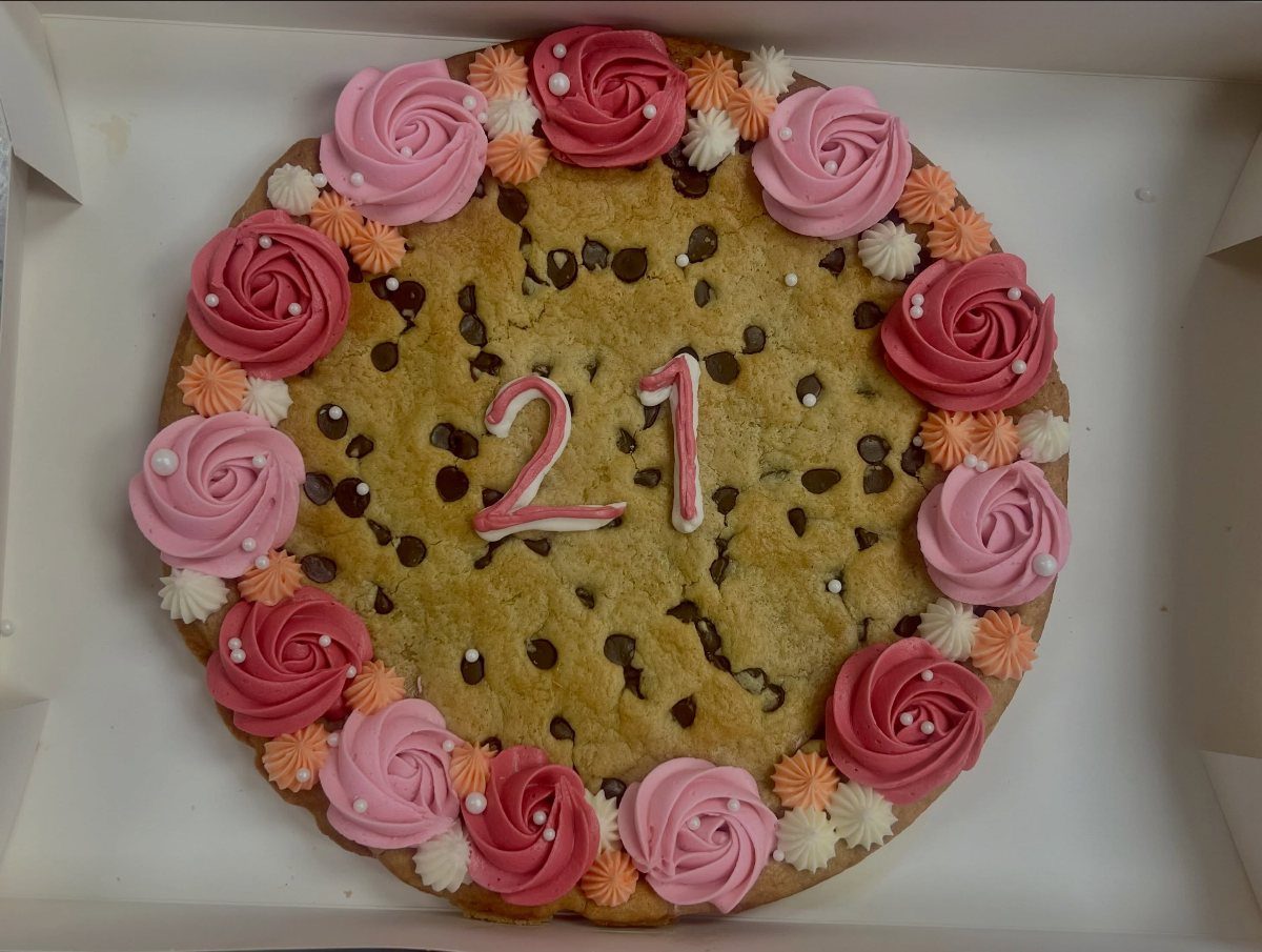 Chocolate chip cookie cake with pink frosting roses and the number 21