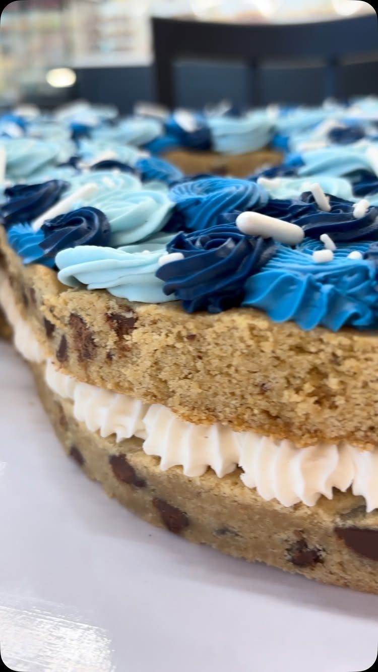 Layered chocolate chip cookie cake topped with blue frosting swirls and white sprinkles.