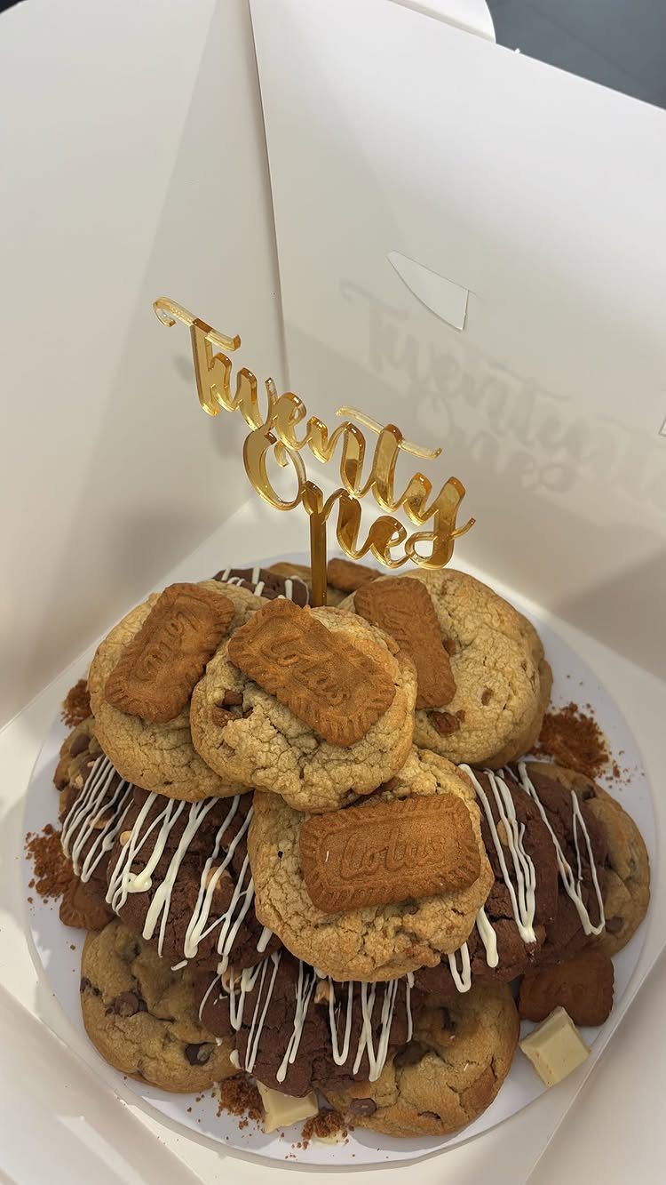Stack of chocolate chip cookies with white drizzle and gold Twenty One topper.
