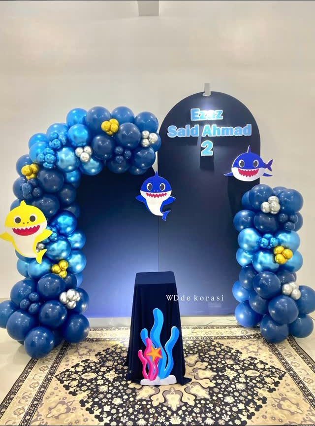 Blue balloon arches and shark decorations for a second birthday party backdrop.