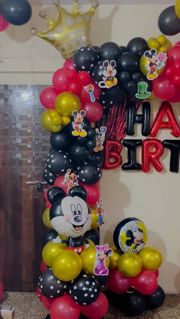 Mickey Mouse themed balloon arch with red, black, and gold balloons and character cutouts.