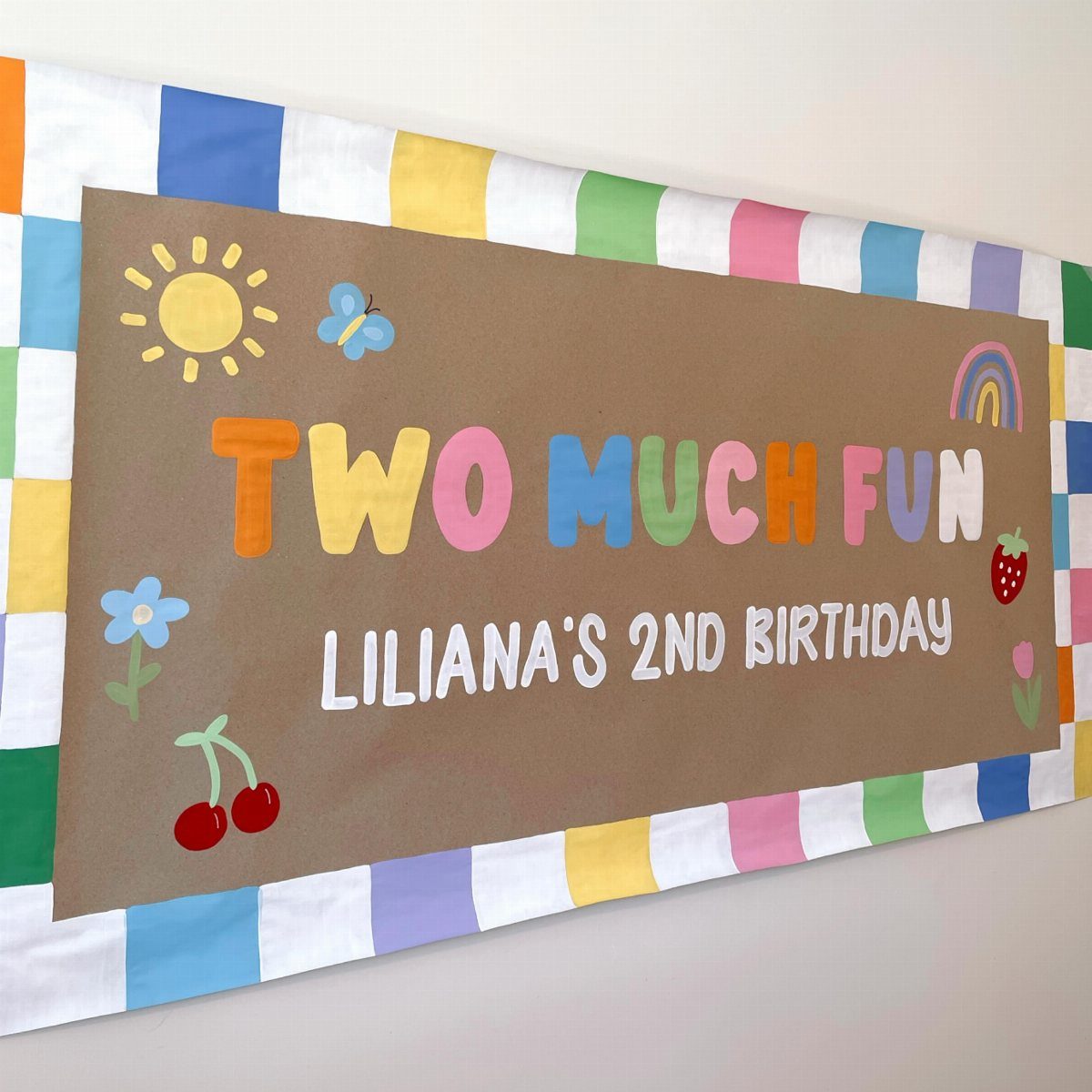 Brown birthday banner with colorful text and fruit illustrations on checkered fabric.