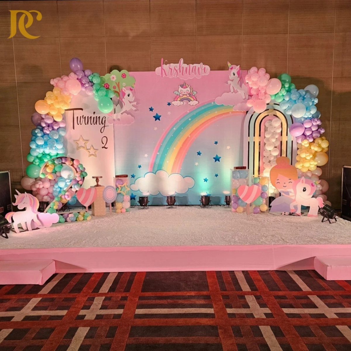 Rainbow birthday party setup with pastel balloon arches and unicorn decorations on stage