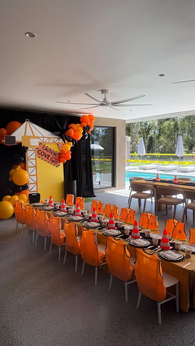 Construction themed party table with orange chairs, traffic cones, and a crane backdrop.