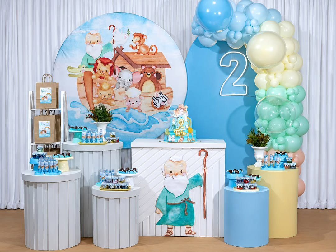 Noah's Ark birthday party setup with animal backdrop, blue balloons, and treat pedestals.