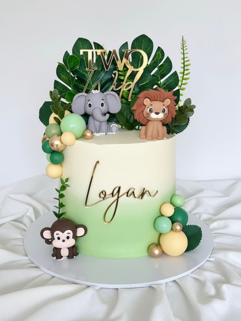 Safari themed birthday cake with animal figures, tropical leaves, and gold Two Wild topper